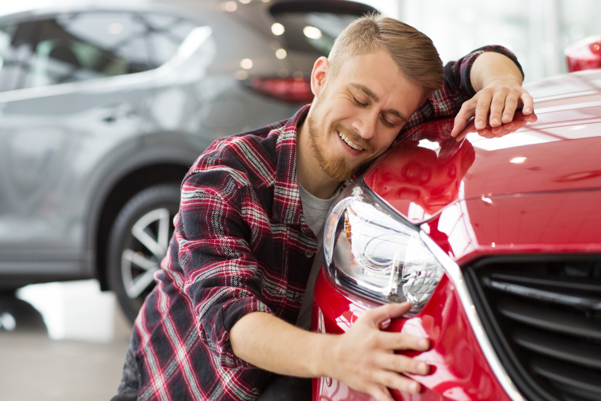 man smiling and hugging the hood of his vehicle