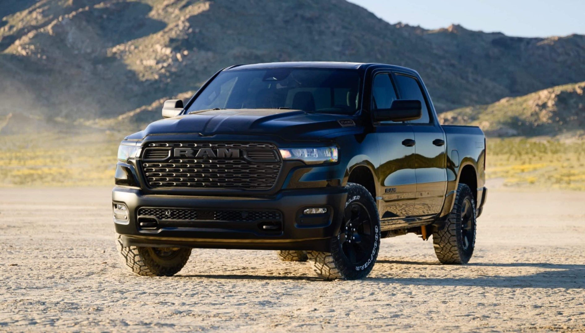 A black RAM 1500 parked off-road in a desert with hills in the background.
