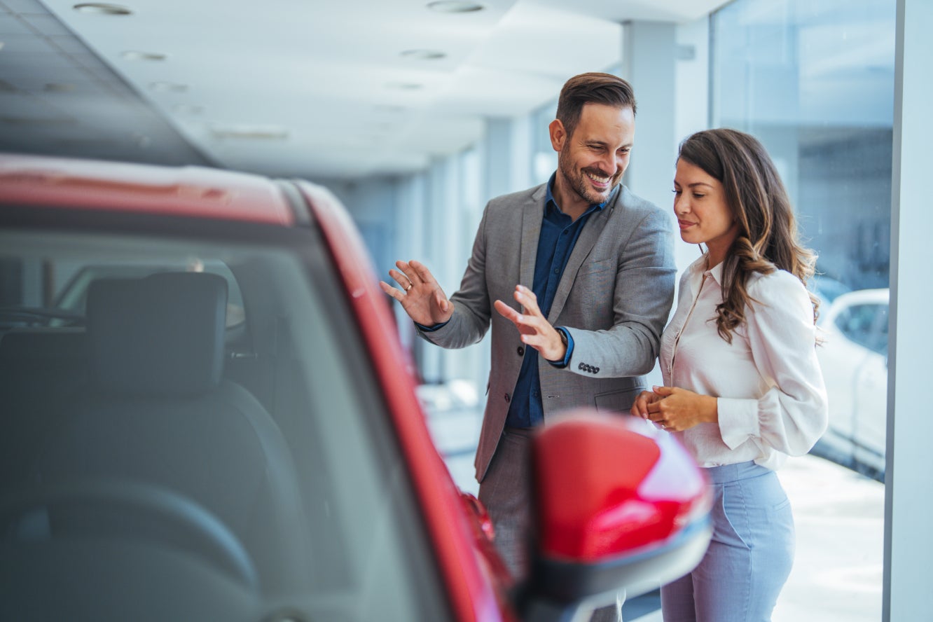 A car salesman showing off a red car to a woman.