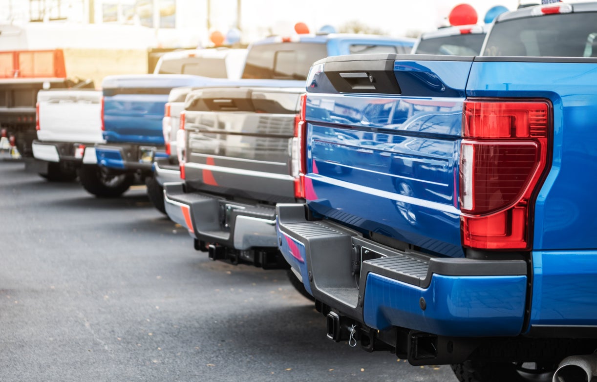 A rear view of a row of pickup trucks on a dealership lot.