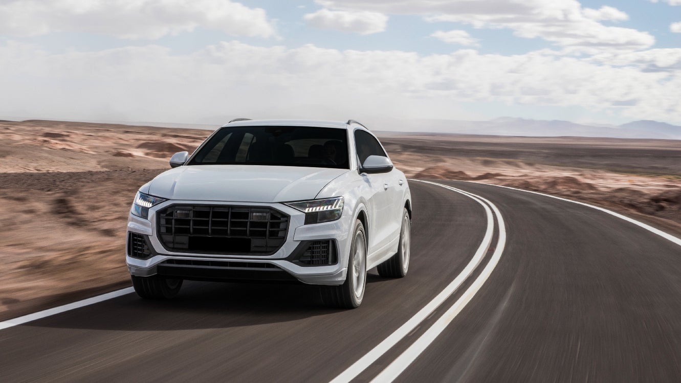 A front view of a white SUV driving on the road through a desert.