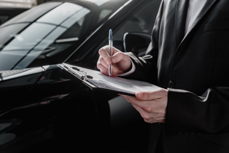 A person signing a vehicle contract while standing beside a black car.