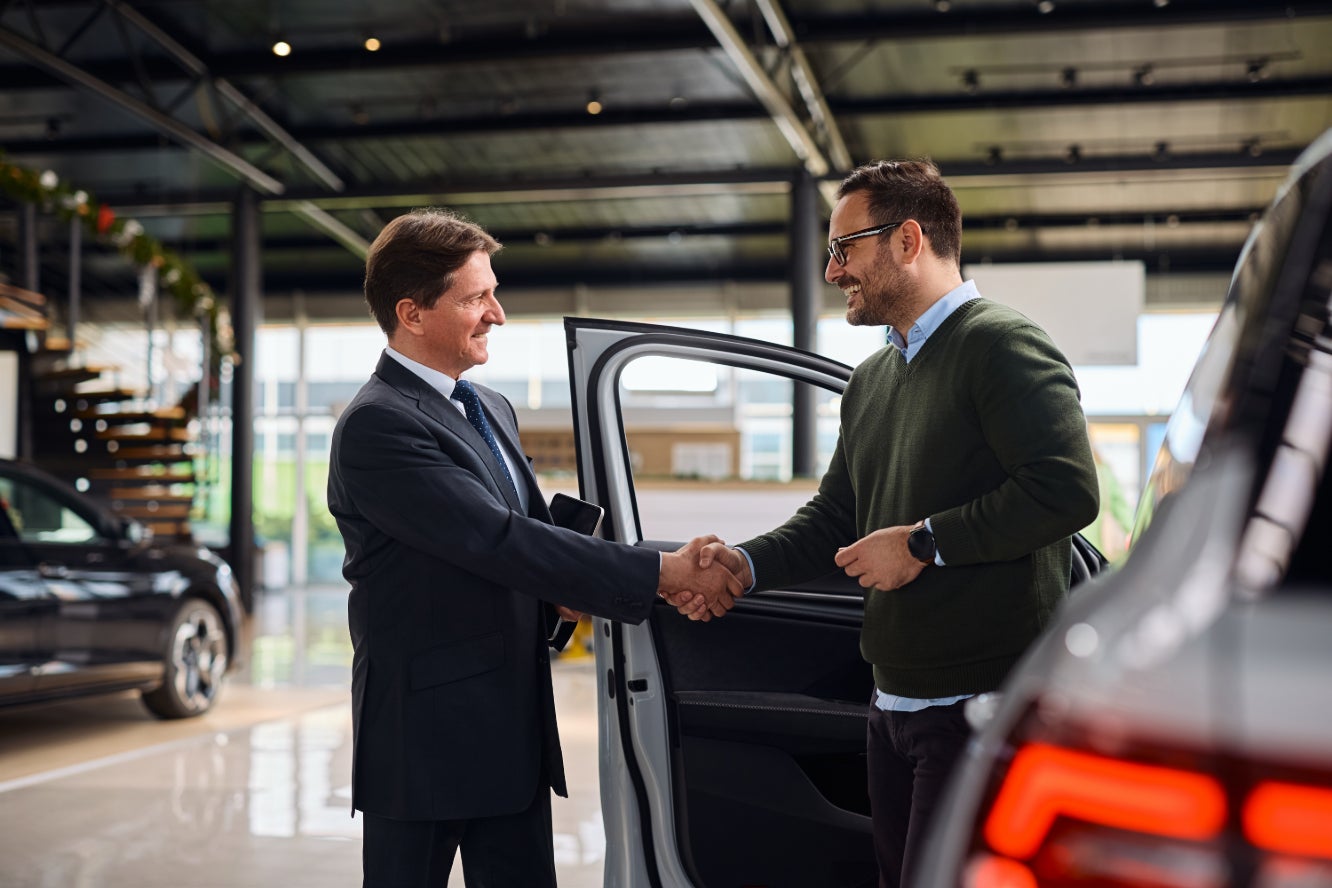 A salesperson shaking hands with a customer after selling them a car.